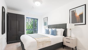 Un dormitorio moderno con una cama grande, una mesita de noche, un armario y una ventana con vistas a zonas verdes.