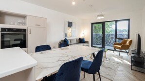 Una cocina moderna con encimera de mármol, un comedor con sillas azules, un sofá con cojines y un mueble para televisor.