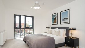 Un dormitorio moderno con una cama grande, una mesita de noche con lámpara y dos cuadros en la pared.