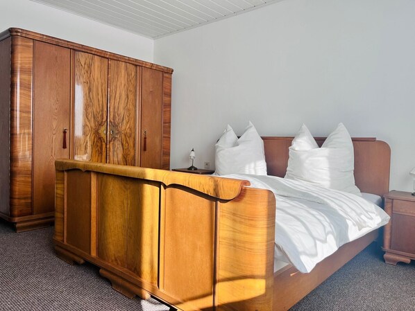 Ein Schlafzimmer mit einem hölzernen Bett, weißer Bettwäsche, einem Nachttisch und einem großen Holzschrank.