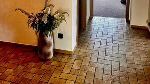 A hallway with a tiled floor, a potted plant, and a view into a room with a blue chair and a window. - Apartment 'Natascha' with Mountain View, Shared Terrace and Wi-Fi (Fellen)