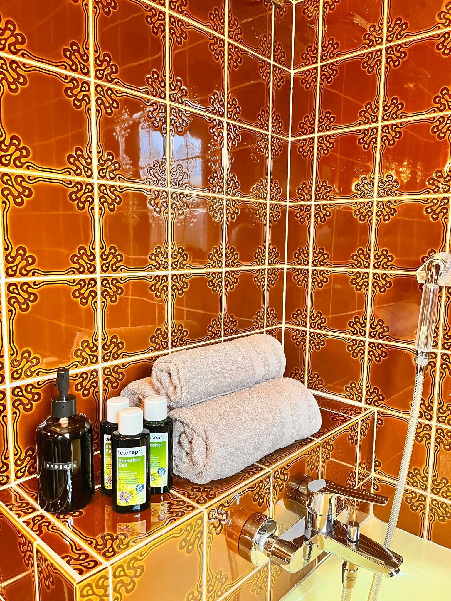 Ein Badezimmer mit aufwendigen, orangefarbenen Fliesen, einem Handtuchhalter mit Handtüchern und Toilettenartikeln auf der Ablagefläche.
