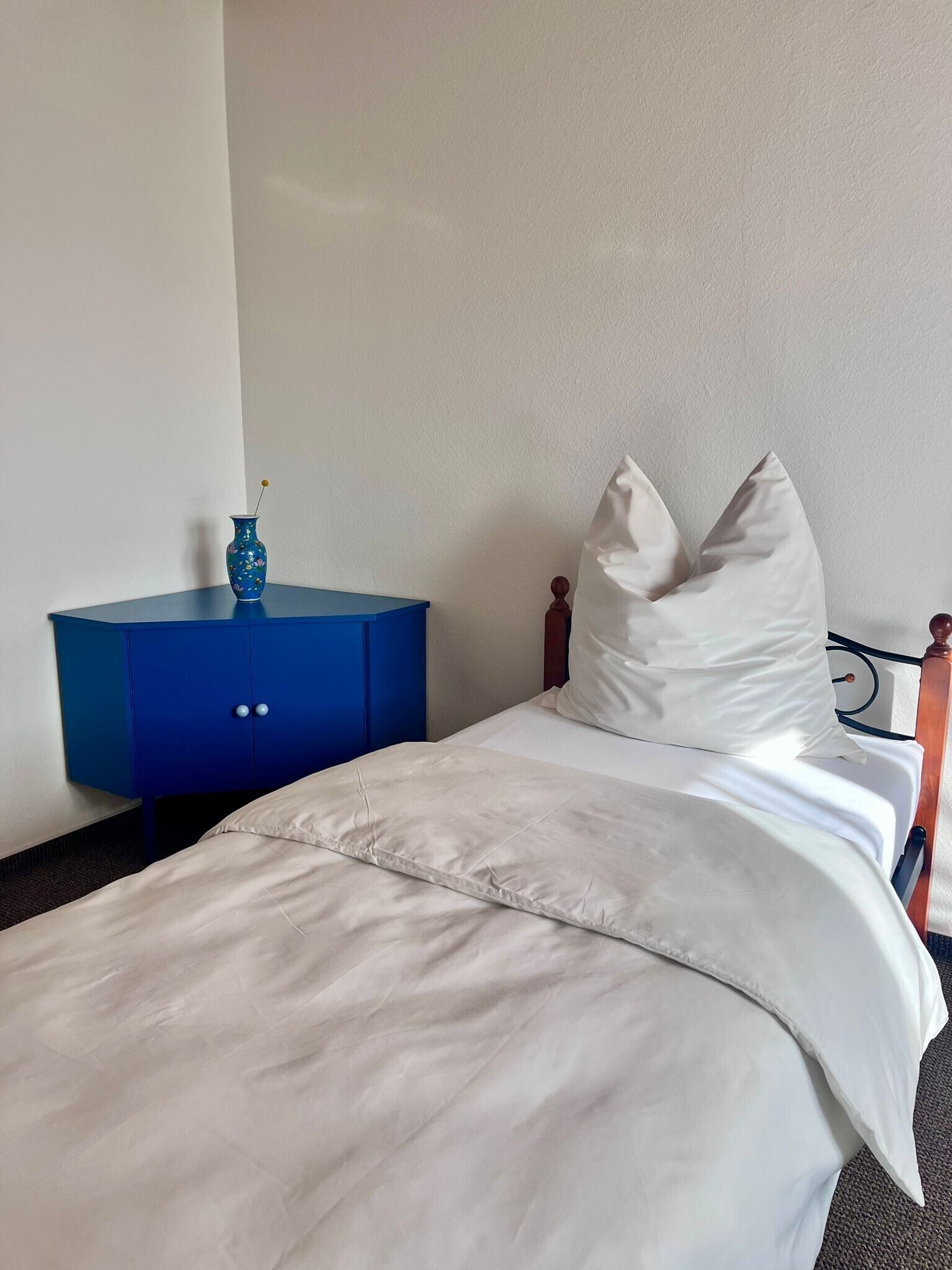Une chambre d’hôtel avec un lit, une table de chevet bleue et un oreiller blanc.