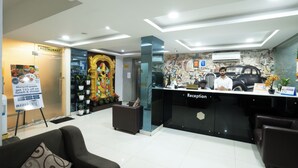 A hotel reception area with a modern design, including a reception desk, seating area, and a wall with a decorative mural. - Hotel Marigold Atnest Gachibowli (Hyderabad)