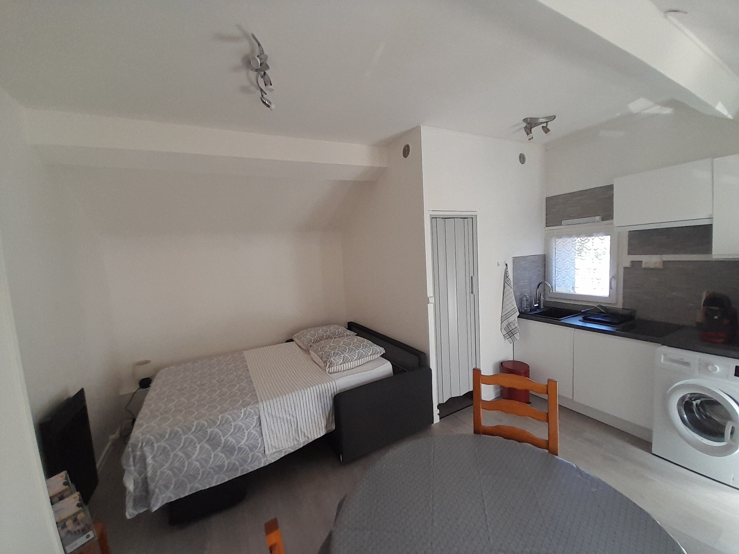 Une petite pièce comprenant un lit, une petite table, une chaise, un lave-linge et un coin cuisine.