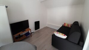 A small, sparsely furnished room with a television, a sofa, and a bed.