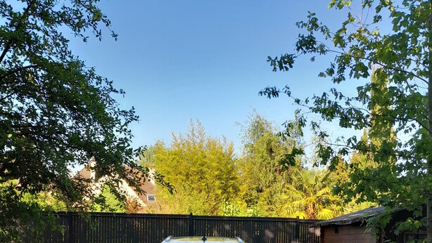 A car parked in a gravel driveway with a black fence and greenery in the background.