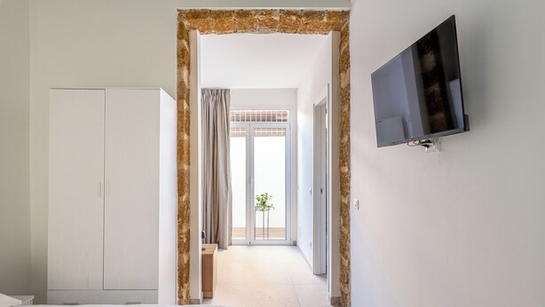 Ett hotellrum med en säng, en garderob, en tv och utsikt över omgivningarna genom en glasdörr.