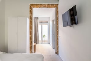 A hotel room with a bed, a wardrobe, a television, and a view of the outside through a glass door.