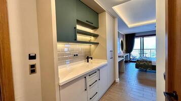 Cocina moderna con encimeras blancas, armarios verdes y vistas a un balcón con mesa y sillas.