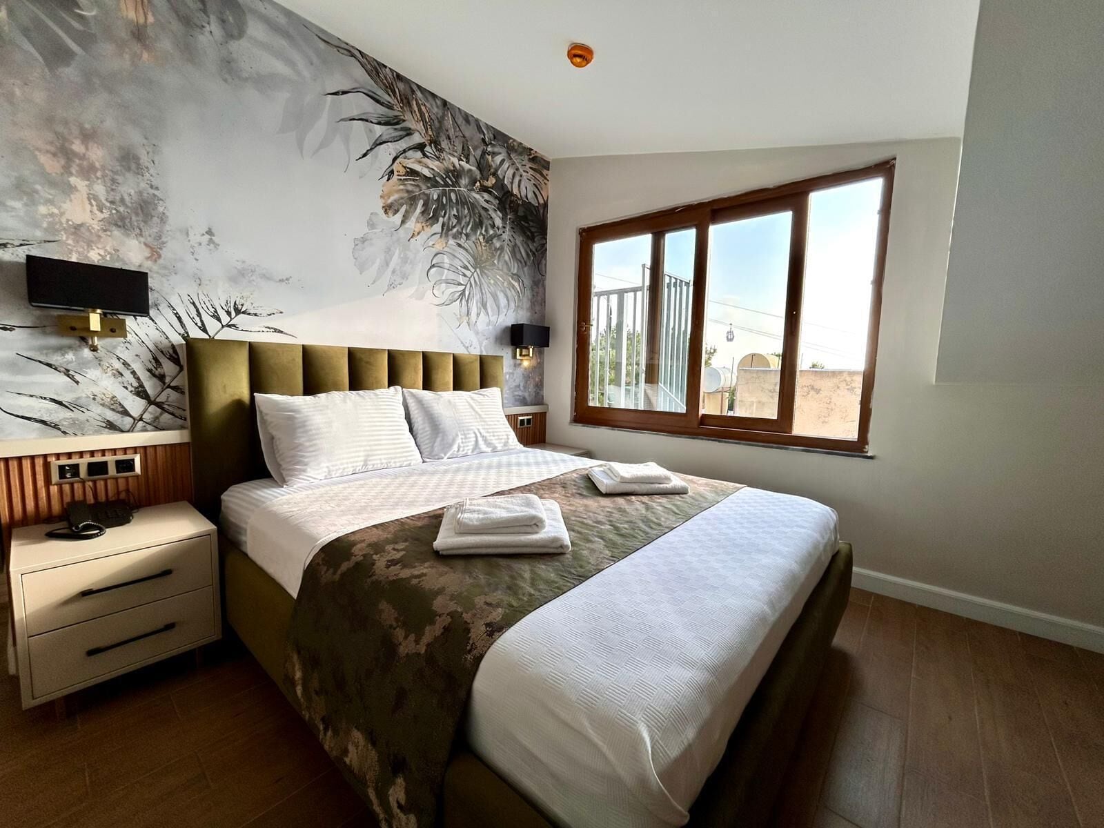 A hotel room with a large bed, a nightstand, a wall-mounted TV, and a window with a view of the desert.