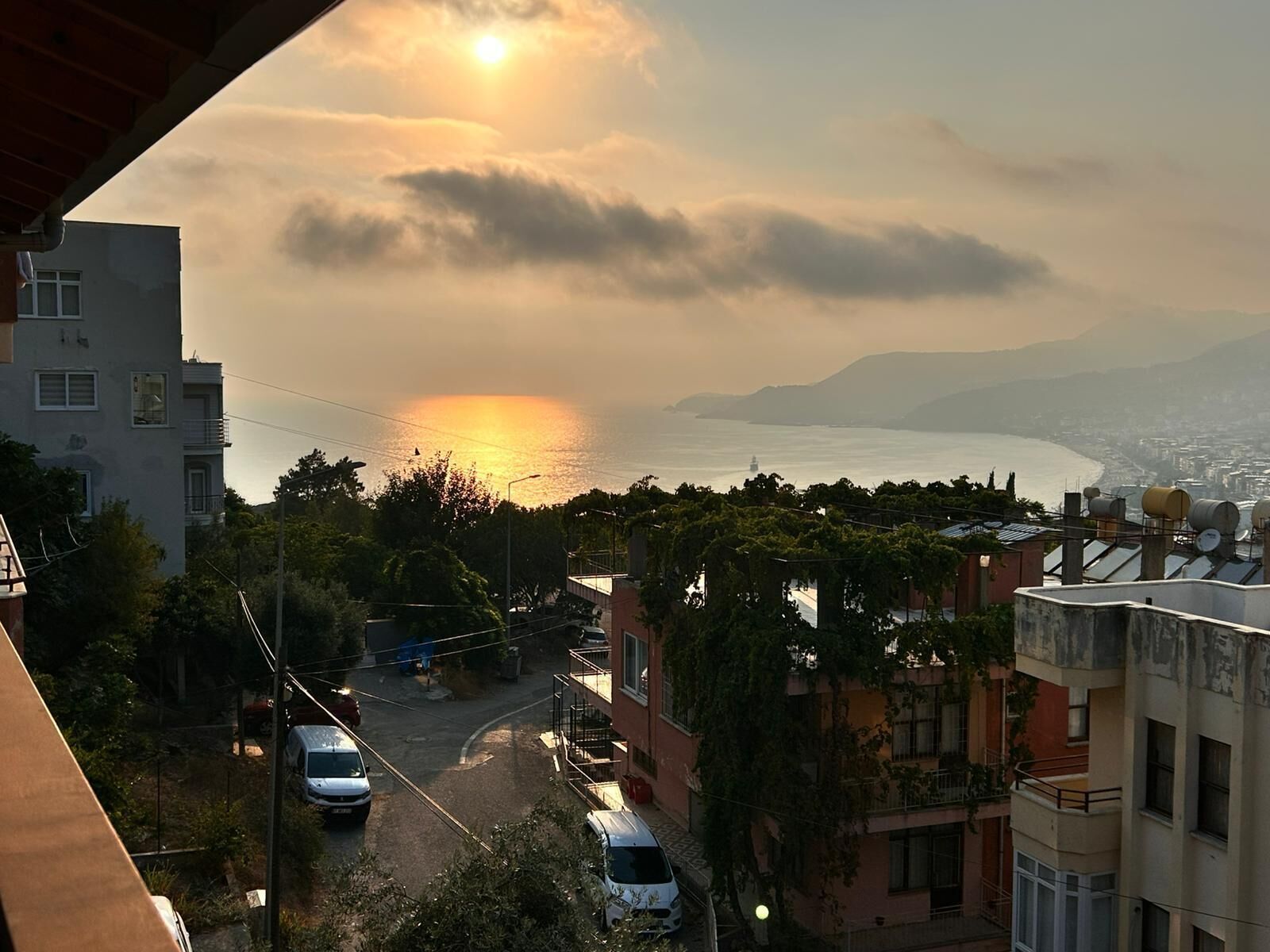 Un paysage urbain côtier avec des bâtiments, une rue et un coucher de soleil sur la mer.