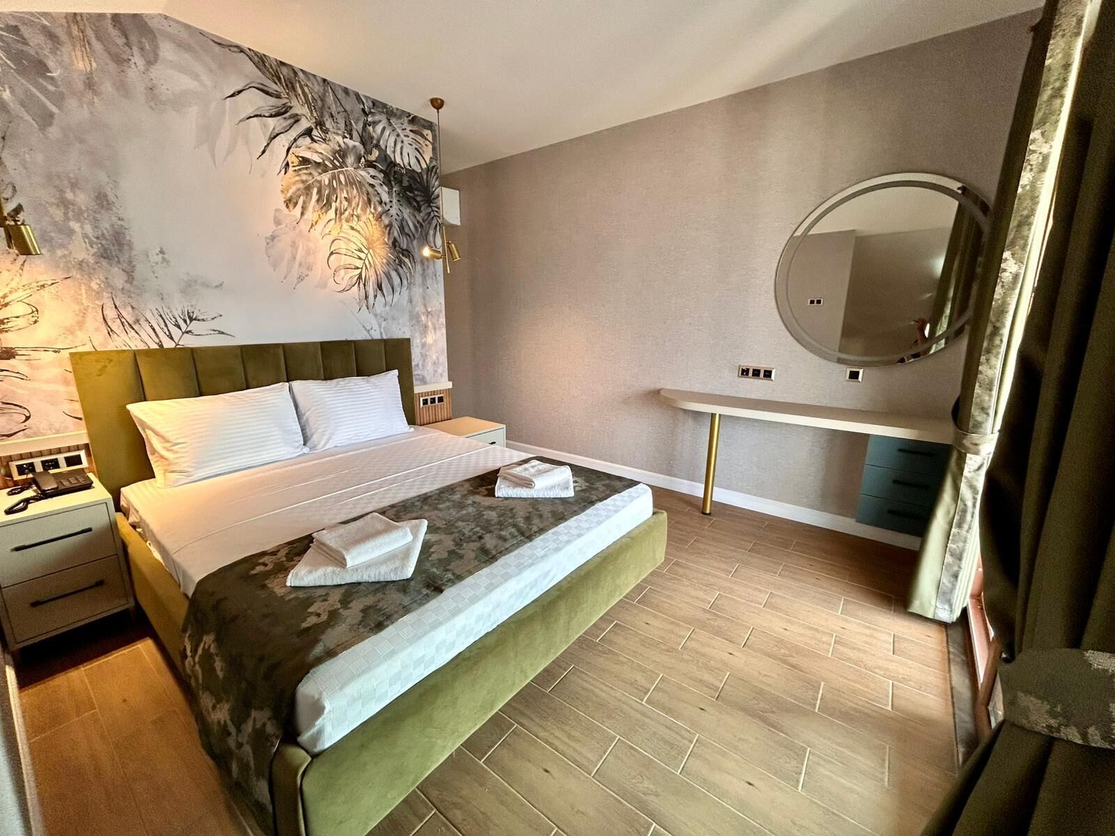 Una camera d'albergo moderna con un letto grande, un comodino, una toeletta con specchio e una parete con motivo a foglia.