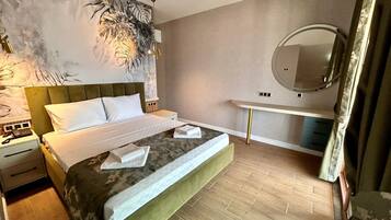 Una camera d'albergo moderna con un letto grande, un comodino, una toeletta con specchio e una parete con motivo a foglia.