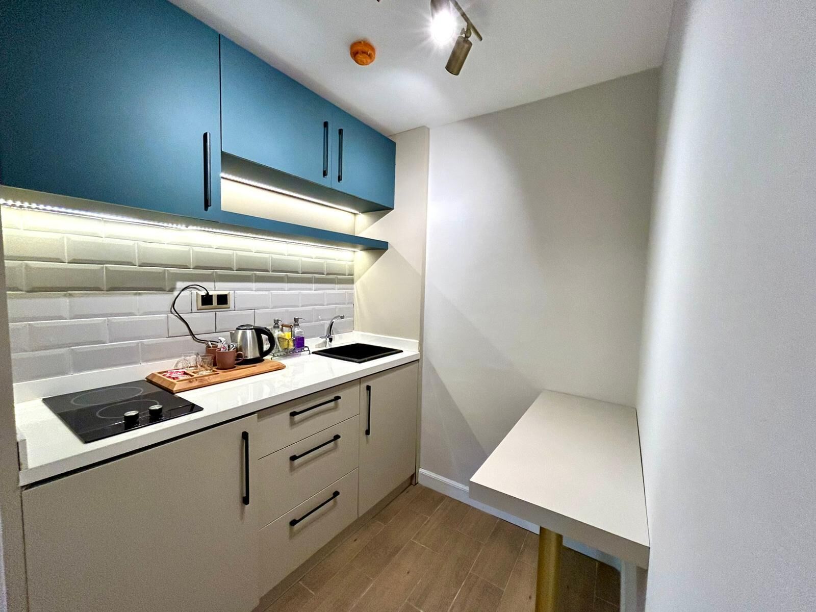 A compact kitchen with blue upper cabinets, a white countertop, a black stove, and a sink.