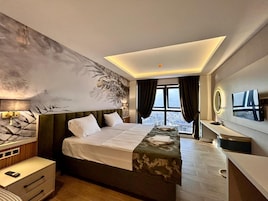 Una habitación de hotel moderna con una cama grande, un escritorio, una tocadora y vistas a la ciudad desde la ventana.