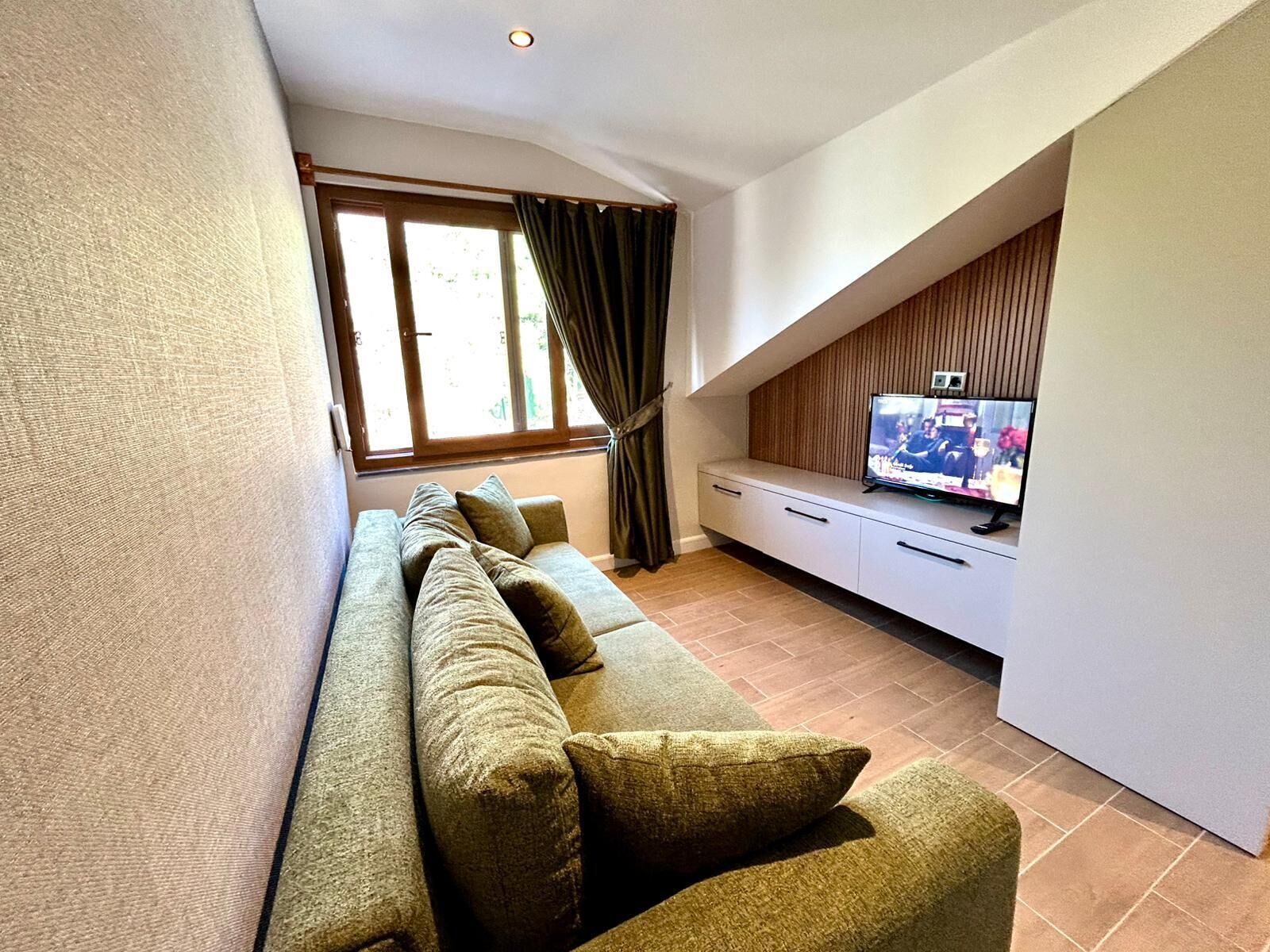 A modern living room with a sofa, a flat-screen TV, and a window with curtains.