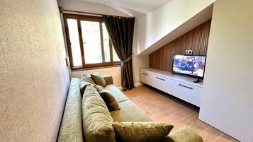 A modern living room with a sofa, a flat-screen TV, and a window with curtains.