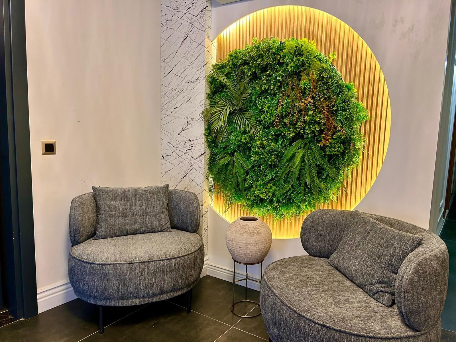 A modern interior with two grey armchairs, a circular wall-mounted green plant, and a textured white wall.