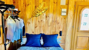 Una habitación de madera con una cama, un perchero y una puerta.