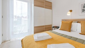 A hotel room with a bed, a nightstand, a lamp, and a view of the outside through a window.