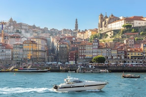 A waterfront cityscape with historic buildings, a prominent church tower, and a busy harbor with boats. - The Morning Light at BoaVista Flats (Porto)