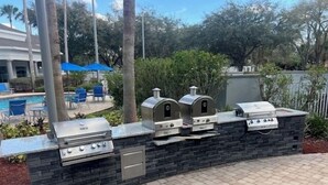 Un espace barbecue avec un mur en pierre, une piscine et des sièges extérieurs.