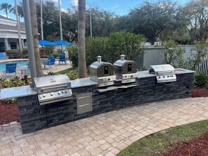 Un espace barbecue avec un mur en pierre, une piscine et des sièges extérieurs.