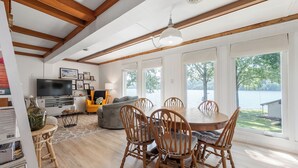 A spacious dining area with a wooden table and chairs, a television, and a sofa in the background. - Lakefront retreat with private dock, open living, fire pit, full kitchen & cozy indoor spaces (Radford)