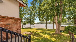 A wooden deck with a brick wall, a grassy area, and a lake view. - Lakefront retreat with private dock, open living, fire pit, full kitchen & cozy indoor spaces (Radford)