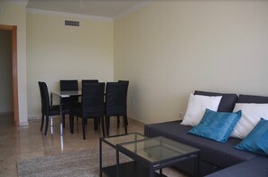 Una sala de estar con un sofá, una mesa de centro de vidrio y un comedor con sillas y una mesa.