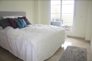 A bedroom with a bed, pillows, a rug, and a view through a window.