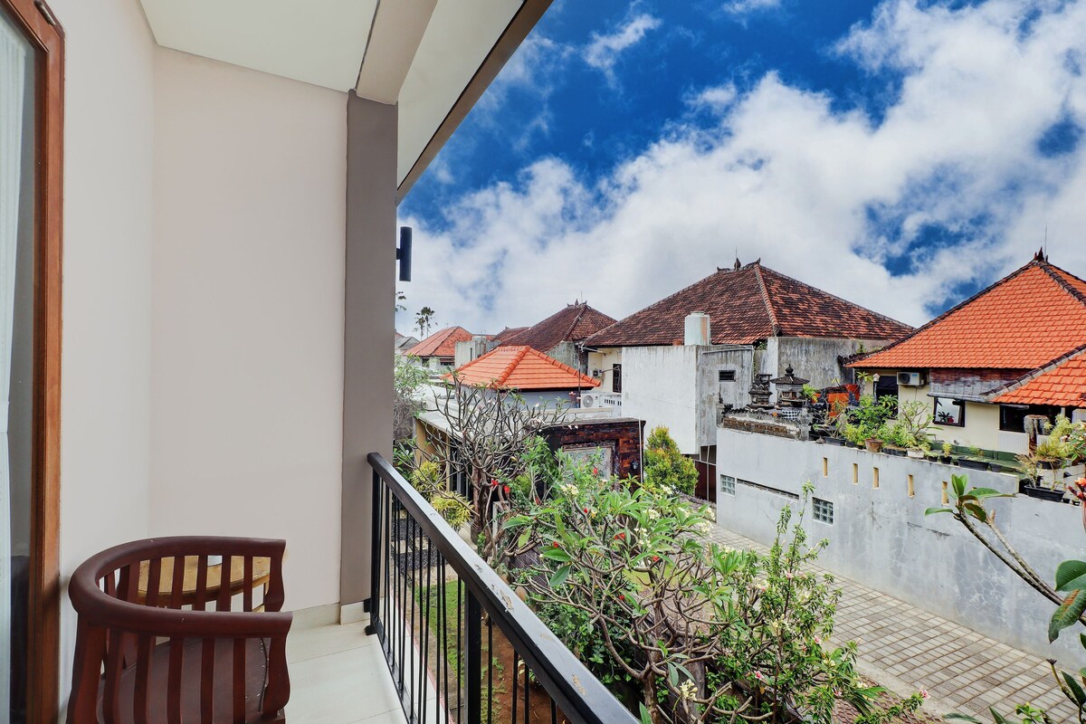 A balcony with a wooden chair, a view of traditional houses with red roofs, and a clear sky.