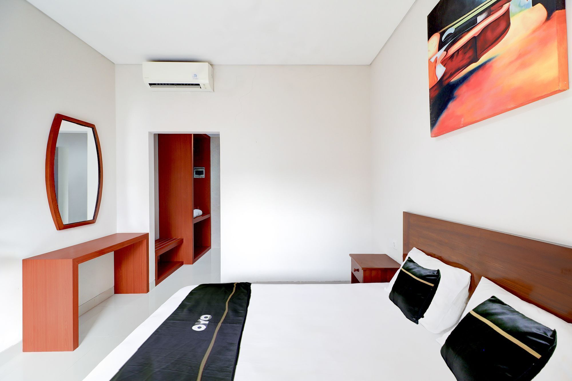Habitación de hotel con cama, mesita de noche, espejo, armario y un cuadro en la pared.