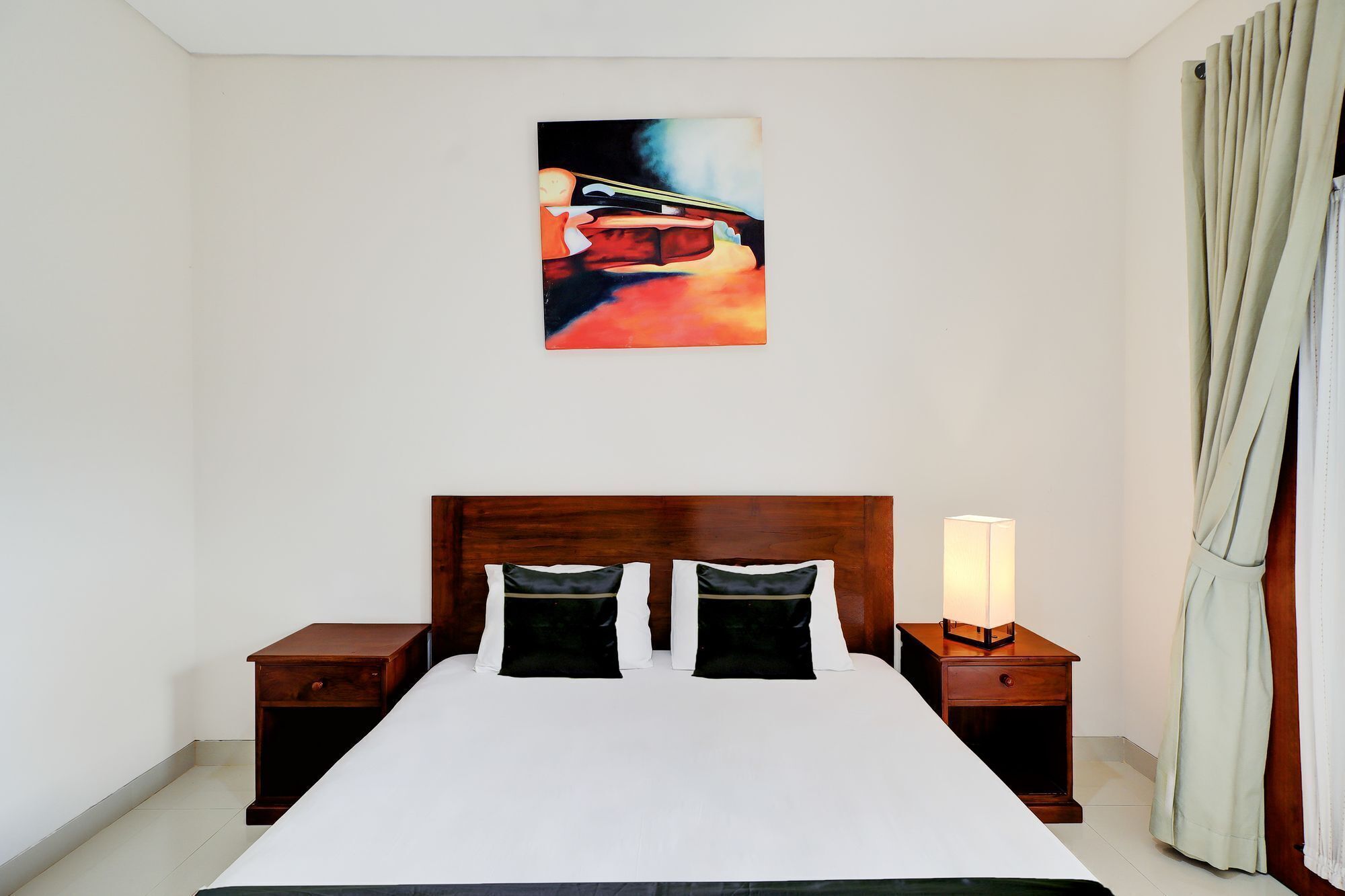 A hotel room with a large bed, two bedside tables, a nightstand with a lamp, and a painting on the wall.