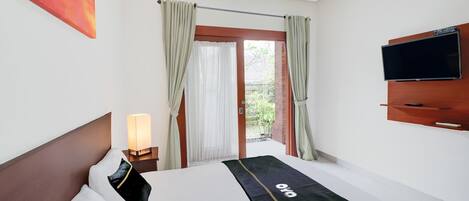 A hotel room with a bed, a TV mounted on the wall, and a window with curtains.