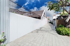 A narrow paved pathway flanked by white walls and a metal fence, leading to a building with a tiled roof. - Collection O Bali Sanur near Bali Mandara Hospital (Denpasar)