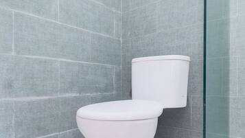 Ein Badezimmer mit Toilette, gefliesten Wänden und einer Duschkabine aus Glas.