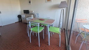 A room with a dining table, chairs, a lamp, a TV, and a fan. - Collioure - Bright studio for 2 people 5 min from the beach (Collioure)