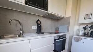 A compact kitchen with white cabinetry, a stainless steel sink, a microwave, a coffee maker, and a small oven. - Collioure - Bright studio for 2 people 5 min from the beach (Collioure)