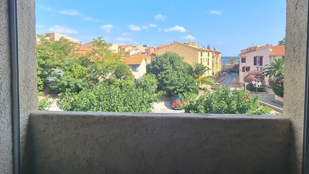 A view from a window with a concrete frame, overlooking a street with buildings and greenery. - Collioure - Bright studio for 2 people 5 min from the beach (Collioure)
