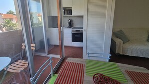 A compact living space with a sliding glass door leading to a balcony, a kitchenette with a microwave and oven, a dining area with a table and chairs, and a bed with a green-striped pillow. - Collioure - Bright studio for 2 people 5 min from the beach (Collioure)