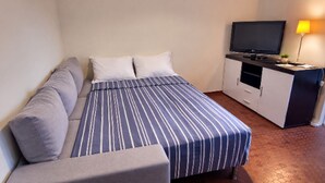A hotel room with a bed, a sofa, a TV, and a desk. - Collioure: T2 Apartment with Terrace and Parking, Sleeps 4 (Collioure)