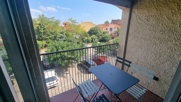 A balcony with a table and chairs, a view of a residential area, and a red car parked outside. - Collioure: T2 Apartment with Terrace and Parking, Sleeps 4 (Collioure)