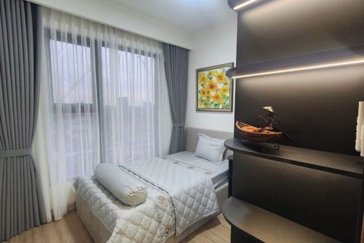 Un dormitorio con una cama, una mesita de noche con lámpara, un cuadro en la pared y una ventana con cortinas.