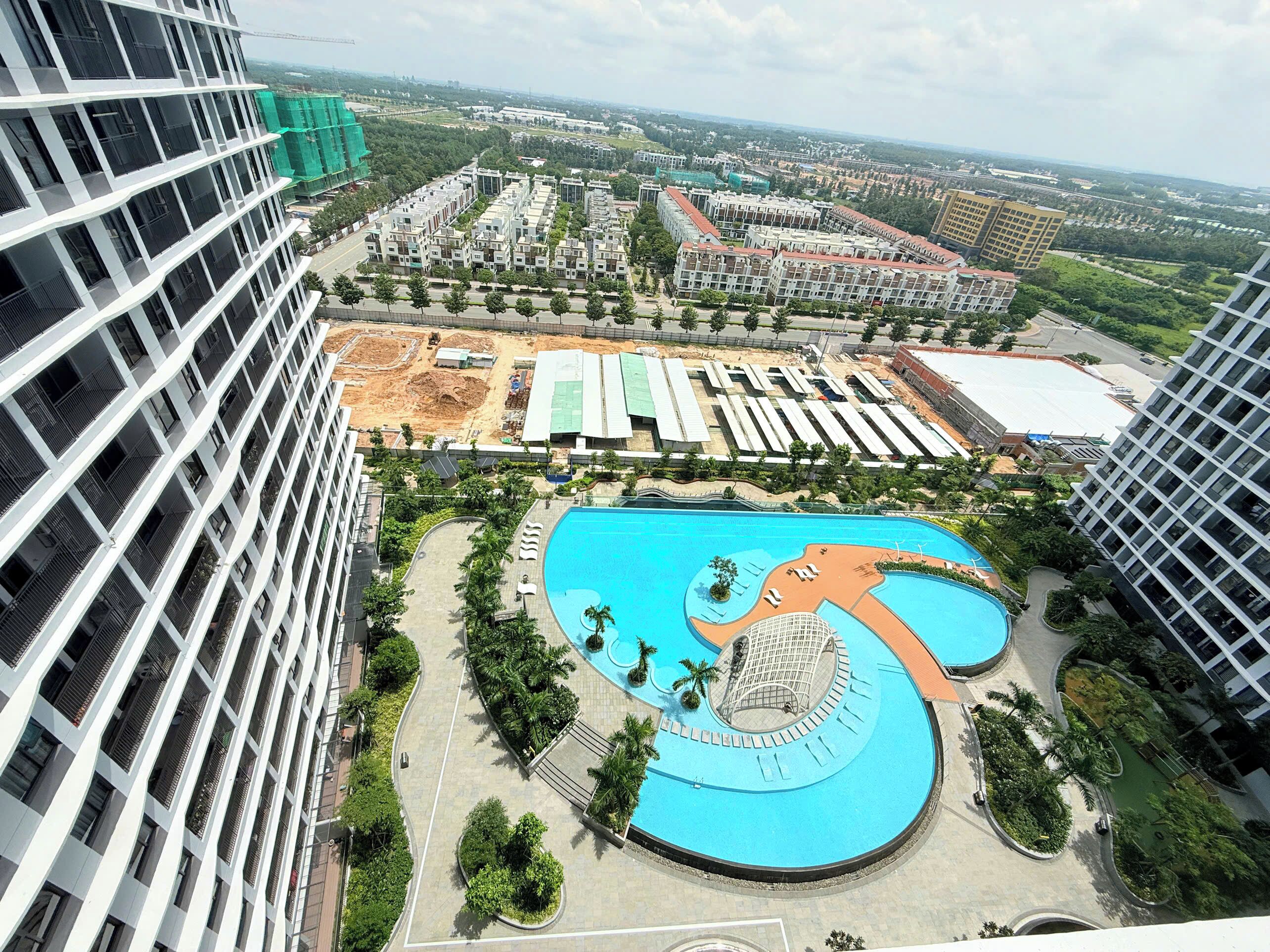 A modern residential complex with a central swimming pool, surrounded by landscaped areas and high-rise buildings.