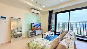 A modern living room with a large flat-screen TV, a sofa, a coffee table, and a balcony with a city view. - Homie's The Glory Apartment (Ho Chi Minh City)