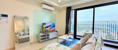 A modern living room with a flat-screen TV, a sofa, a coffee table, and a balcony with a city view.