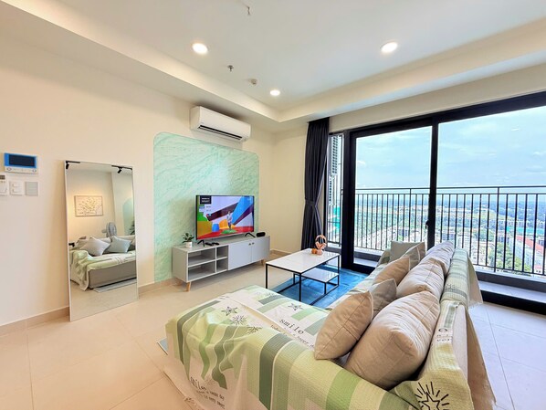 Una sala de estar moderna con una televisión de pantalla plana, un sofá, una mesa de centro y un balcón con vistas a la ciudad.