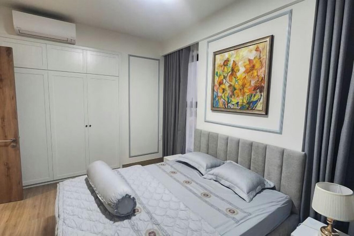 A bedroom with a bed, a nightstand, a lamp, a painting, and a wardrobe.